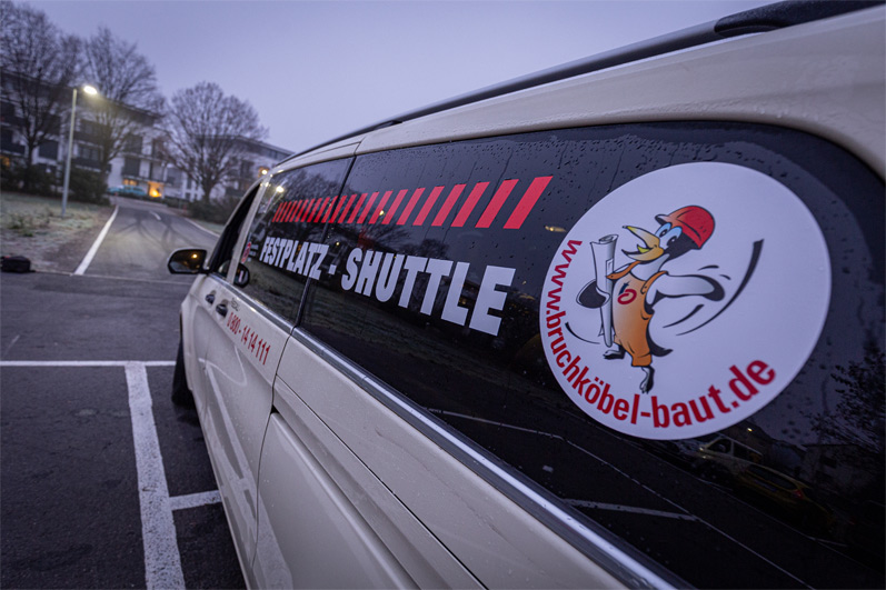 Seitenansicht des Taxis mit dem Schriftzug Baustellen-Shuttle und einem Bild von Pingus, dem baustellen-Maskottchen.